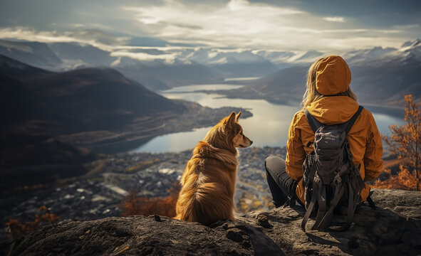 Cinematic image of a hiker girl with her dog at the top of the mountain with rocks, autumn trees and lake. Long shot of a beautiful scene in autumn from the top.