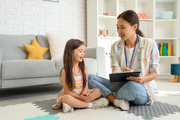 Female Asian speech therapist writing on clipboard and little girl in office