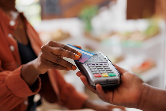 Black person using credit card to make contactless payment for fresh organic produce at a local market. Closeup of african american customer doing cashless transaction at grocery store - Powered by Adobe
