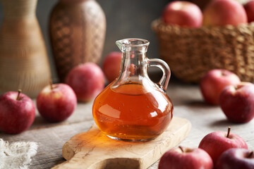A glass jug of apple cider vinegar with fresh apples on a table