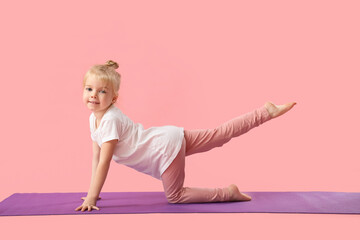 Cute little girl practicing yoga on mat against pink background