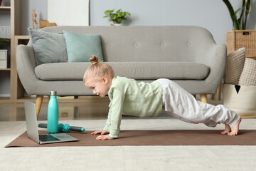 Cute little girl practicing yoga on mat while watching online tutorial in living room