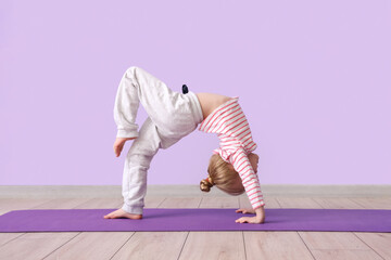 Cute little girl practicing yoga on mat against lilac background - Powered by Adobe