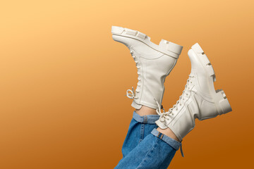 Female legs in white combat boots and blue jeans upside down on blue background, side view. Woman wearing trendy military beige shoes on high platform with laces. Seasonal female fashion