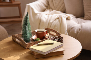 Wooden coffee table with books, mini Christmas trees and cup of tea in interior of light living room