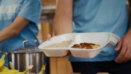 Close-up on caucasian man serving bread chicken and baked beans to poor hungry person at food drive. Detailed view of meal box from hunger relief team given to the needy. Selective-focus handheld.