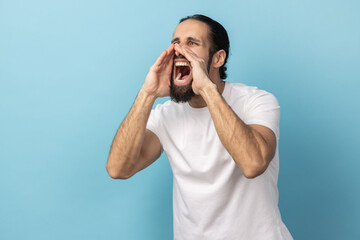 Side view portrait of man with beard wearing white T-shirt standing and screaming about bad news or...