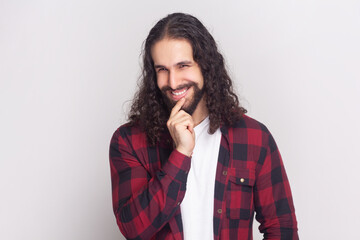 Portrait of man with long curly hair in checkered red shirt looking with cunning eyes holding her...