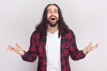 Portrait of Aggressive outraged bearded man with long curly hair in checkered red shirt gestures...
