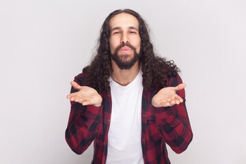 Portrait of pleased bearded man with long curly hair in checkered red shirt stretches hands near...