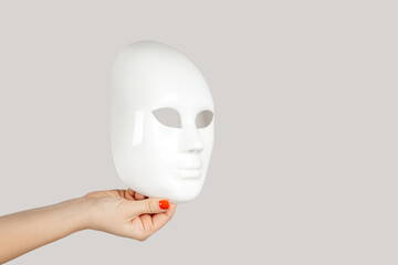 Closeup of woman hand showing white mysterious mask, hiding personality. Indoor studio shot isolated on gray background. - obrazy, fototapety, plakaty