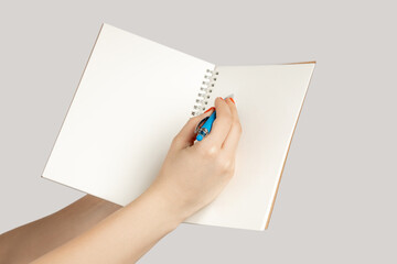 Closeup of woman hand showing open notebook with empty pages, writing with pen, copy space. Indoor studio shot isolated on gray background.