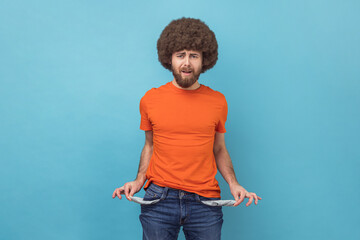 Portrait of man with Afro hairstyle wearing orange T-shirt showing empty pockets of his pants,...