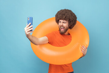 Man with Afro hairstyle wearing orange T-shirt holding orange rubber ring and cell phone, having...