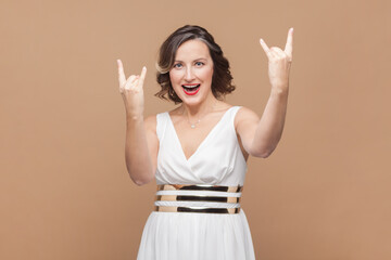 Hey, rock on. Crazy woman with wavy hair makes rock n roll gesture, stands excited and cheerful,...