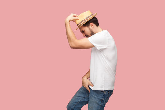 Portrait of handsome bearded hipster man in white shirt and casual hat standing in michael jackson dancing pose, being in good happy mood. Indoor studio shot isolated on pink background.