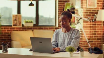 African american woman writing blog article at home, catching sunset light while she is solving...