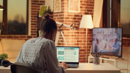 Obraz premium Freelancer studying data for research, preparing to solve new online tasks for marketing and sales segment. African american woman providing freelance services from home, sunset hour.