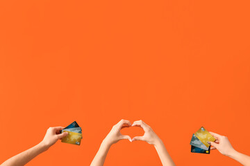Women with credit cards making heart gesture on orange background