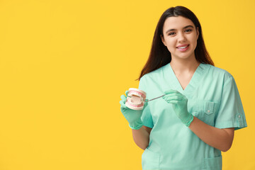 Female dentist with jaw model and tool on yellow background. World Dentist Day