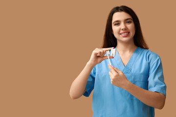 Female dentist with toothbrush and plastic tooth on brown background. World Dentist Day