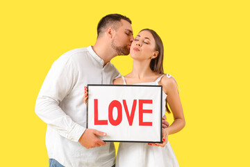 Lovely couple holding frame with word LOVE on yellow background. Valentine's Day celebration