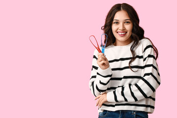 Happy young Asian woman with tongue scrapers on pink background