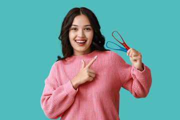 Young Asian woman pointing at tongue scrapers on blue background