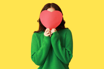 Young Asian woman with red paper heart on yellow background. Valentine's Day celebration
