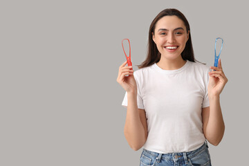 Young woman with tongue scrapers on light background