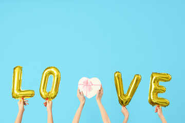 Female hands holding heart-shaped gift box and word LOVE made from balloons on blue background....