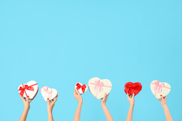 Female hands holding different heart-shaped gift boxes on blue background. Valentine's Day...