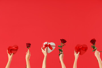 Female hands holding heart-shaped gift boxes and roses on red background. Valentine's Day...