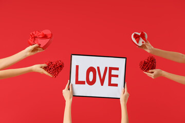 Female hands holding frame with word LOVE, gift boxes and hearts on red background. Valentine's Day...