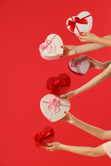 Female hands holding different heart-shaped gift boxes on red background. Valentine's Day celebration