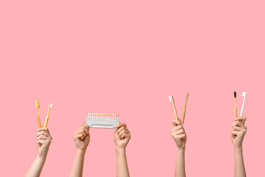 Female hands with toothbrushes and dental shade guide on pink background