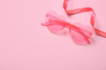 Pink heart shaped sunglasses with ribbon on color background. Valentine's Day concept