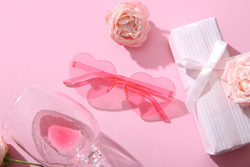 Pink heart shaped sunglasses with gift box, glass and roses on color background. Valentine's Day concept