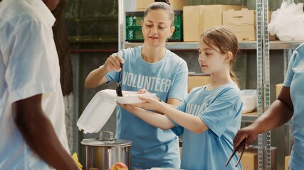 Focus on caucasian mother and daughter helping out during food drive, distributing free food to...