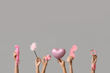 Many female hands with heart shaped balloon and sex toys on grey background. Valentine's Day celebration