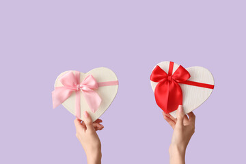 Female hands with gift boxes in shape of heart on lilac background. Valentine's Day celebration