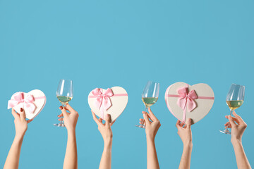 Women with glasses of wine and gift boxes on blue background. Valentine's Day celebration