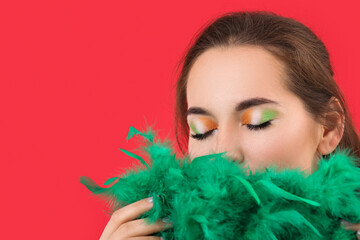 Young woman with green feather boa and makeup for St. Patrick's Day on red background