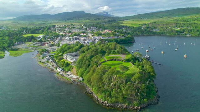 AERIAL: Picturesque seaside town with harbour on the Isle of Skye on a sunny day. Charming Portree in a sheltered part of the coast of a hilly and green island. Beautiful scenery in northern Scotland.