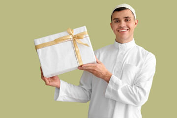 Young Muslim man with gift box on green background. Ramadan celebration