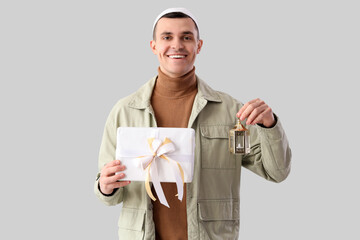 Young Muslim man with gift box and lamp on light background. Ramadan celebration