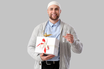 Young Muslim man with glass of water and gift on light background. Ramadan celebration