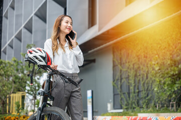 A smiling businesswoman helmeted and holding her smartphone strikes a balance between work joy and technology during a bike ride. This modern lifestyle is portrayed in her cheerful expression.