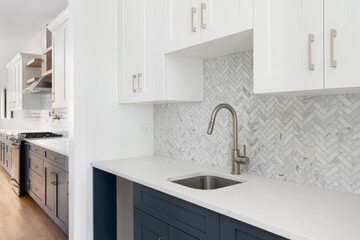 A scullery or butler's pantry detail with a bronze faucet and hardware, blue and white cabinets, and marble herringbone tile backsplash and countertop.