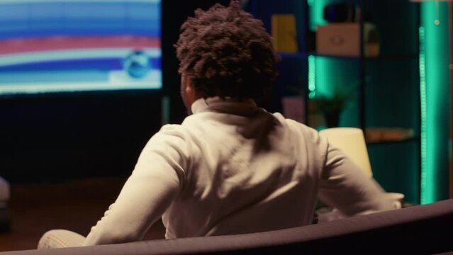 Person relaxing on sofa watching content on multimedia television set in living room. Close up shot on african american man enjoying leisure time in front of smart TV in home theatre